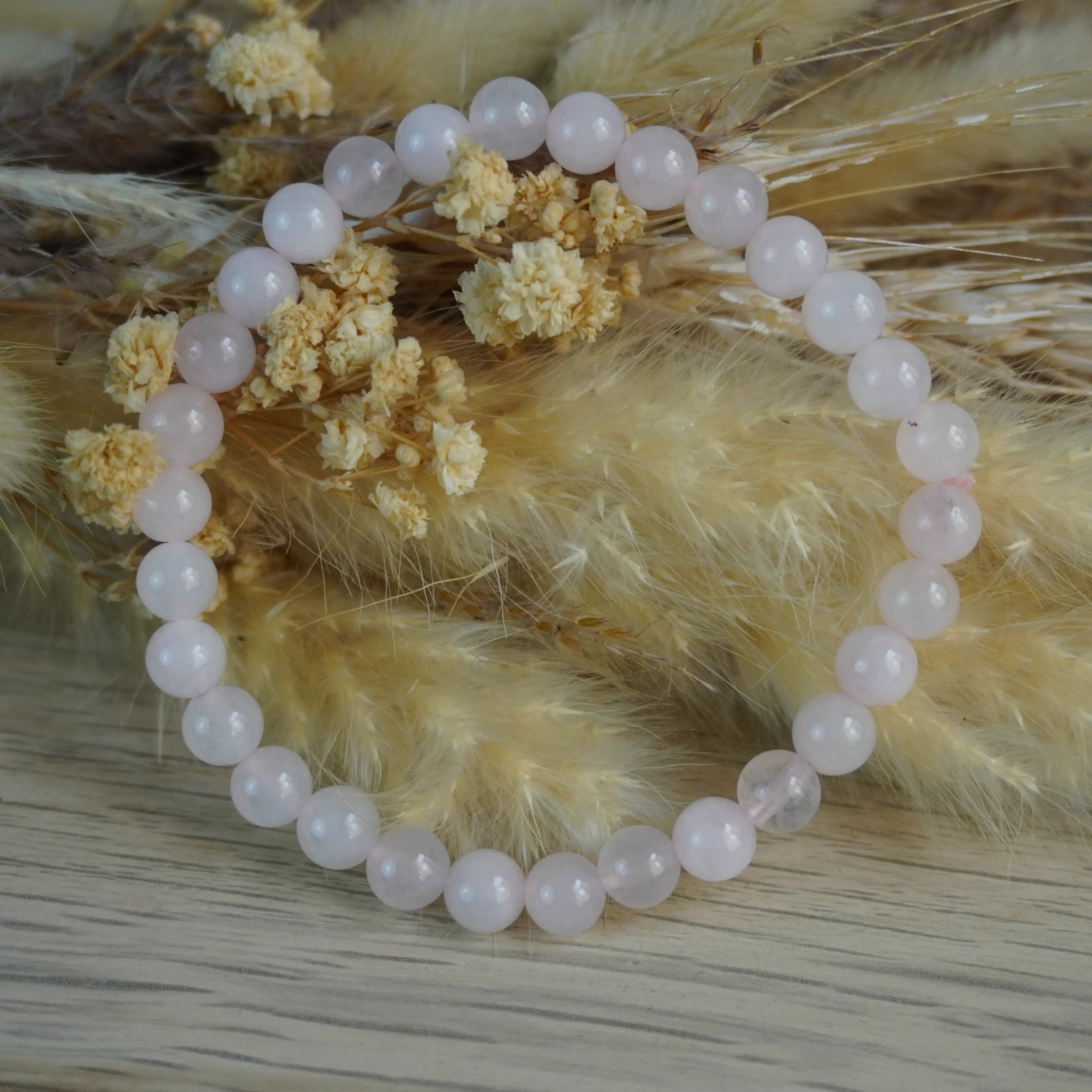 Rosenquarz Kugelarmband vor Trockenblumen Hintergrund
