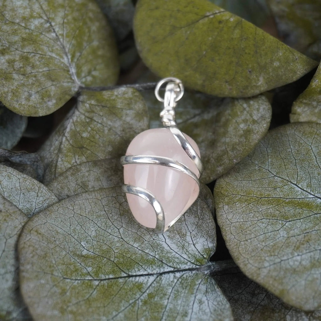 Rosenquarz Kettenanhänger mit silberner Spirale dekoriert auf grünen Eukalyptusblättern