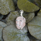 Rosenquarz Kettenanhänger mit silberner Spirale dekoriert auf grünen Eukalyptusblättern