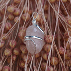 Rosenquarz Kettenanhänger mit silberner Spiralfassung vor rosa Trockenblumen arrangiert