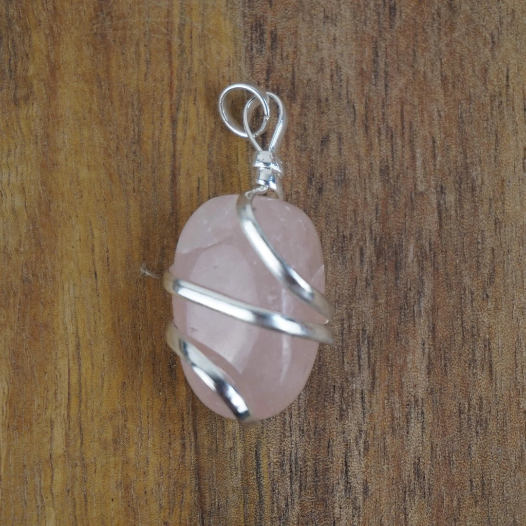 Rosenquarz Kettenanhänger mit silberner Spiralfassung vor Holzuntergrund