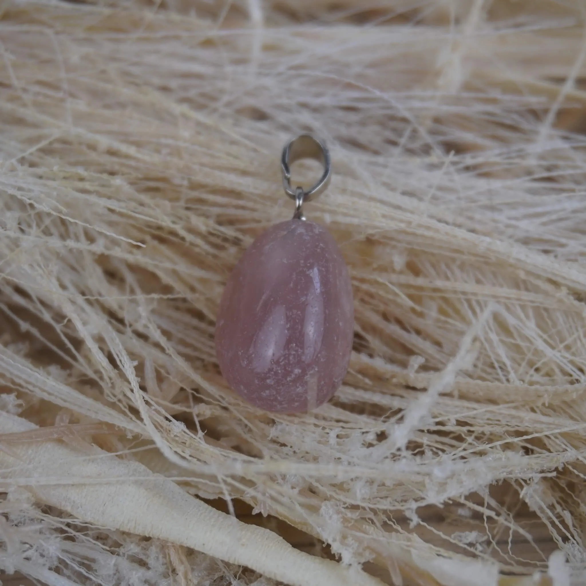 Rosenquarz Kettenanhänger mit silberner Öse auf hellen Naturfasern dekoriert