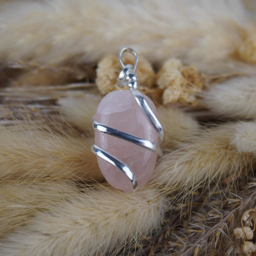 Rosenquarz Kettenanhänger mit Silberfassung auf beigen Trockenpflanzen