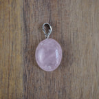 Rosenquarz Kettenanhänger mit silberfarbener Öse vor Holzuntergrund