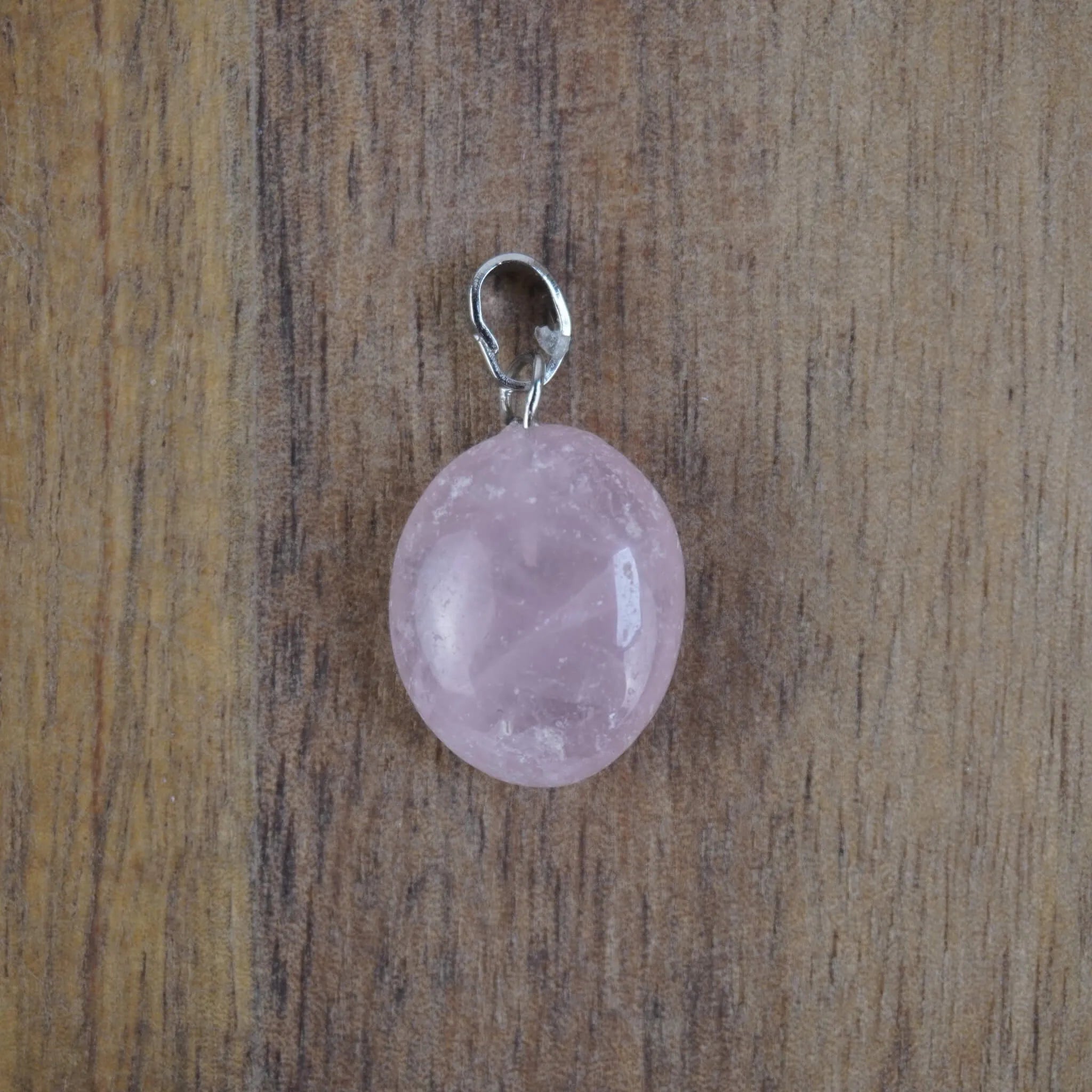 Rosenquarz Kettenanhänger mit silberfarbener Öse vor Holzuntergrund