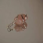 Liegender Rosenquarz Kettenanhänger mit silberner Spiralfassung und Spiegelung auf glänzender Fläche