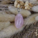 Rosenquarz Kettenanhänger mit silberfarbener Öse auf beigen Trockenpflanzen