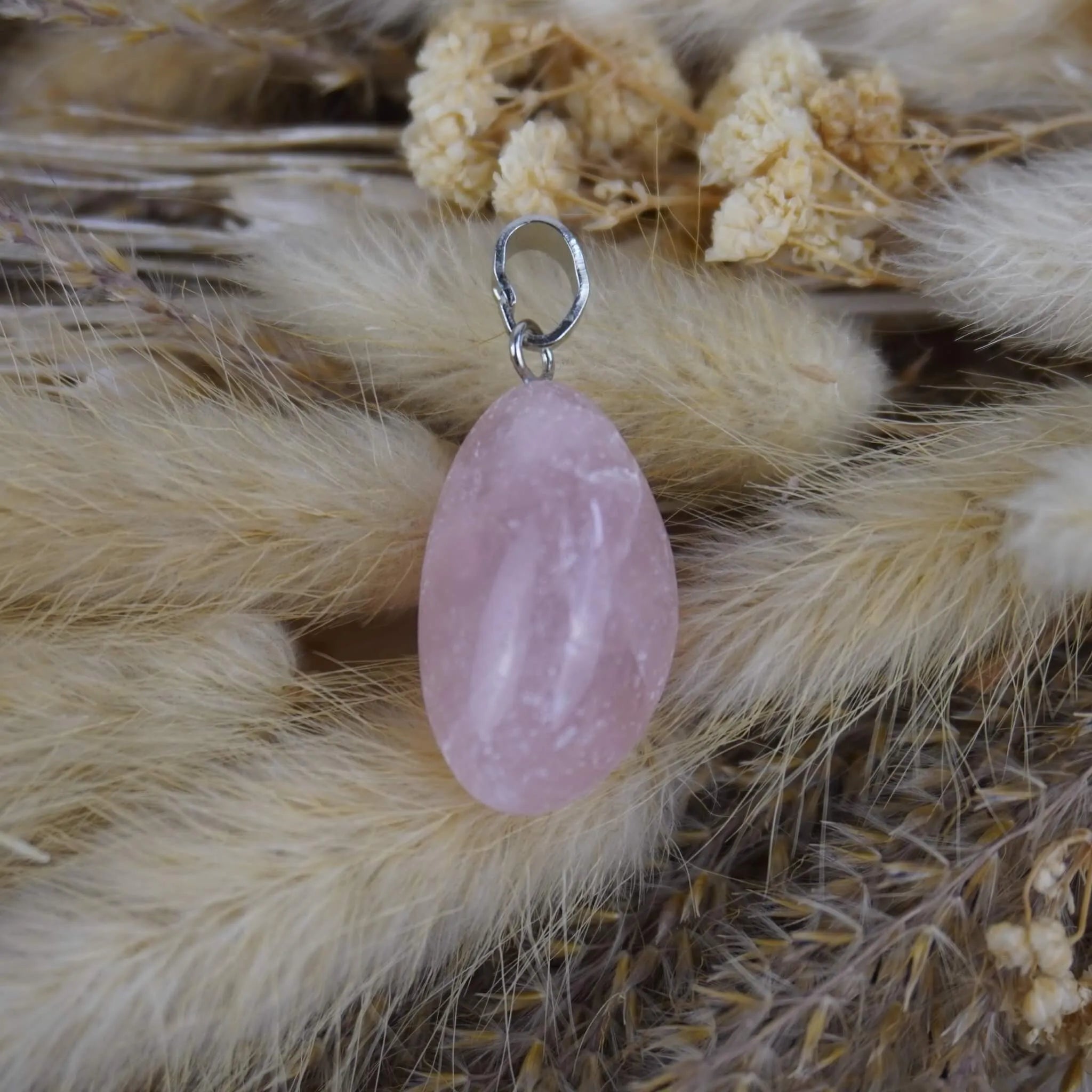 Rosenquarz Kettenanhänger mit silberfarbener Öse auf beigen Trockenpflanzen