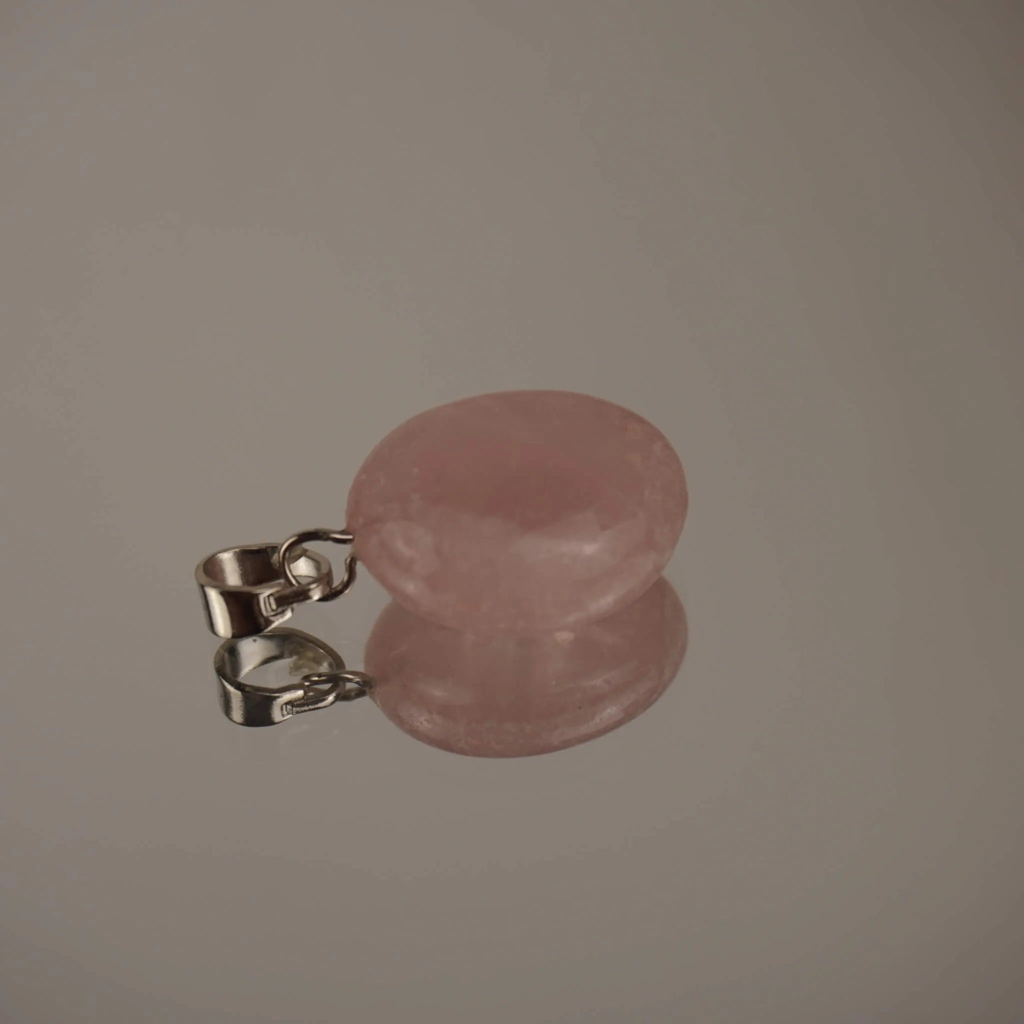 Zartrosa Rosenquarz Trommelstein Kettenanhänger mit silberfarbener Öse auf glänzender Fläche