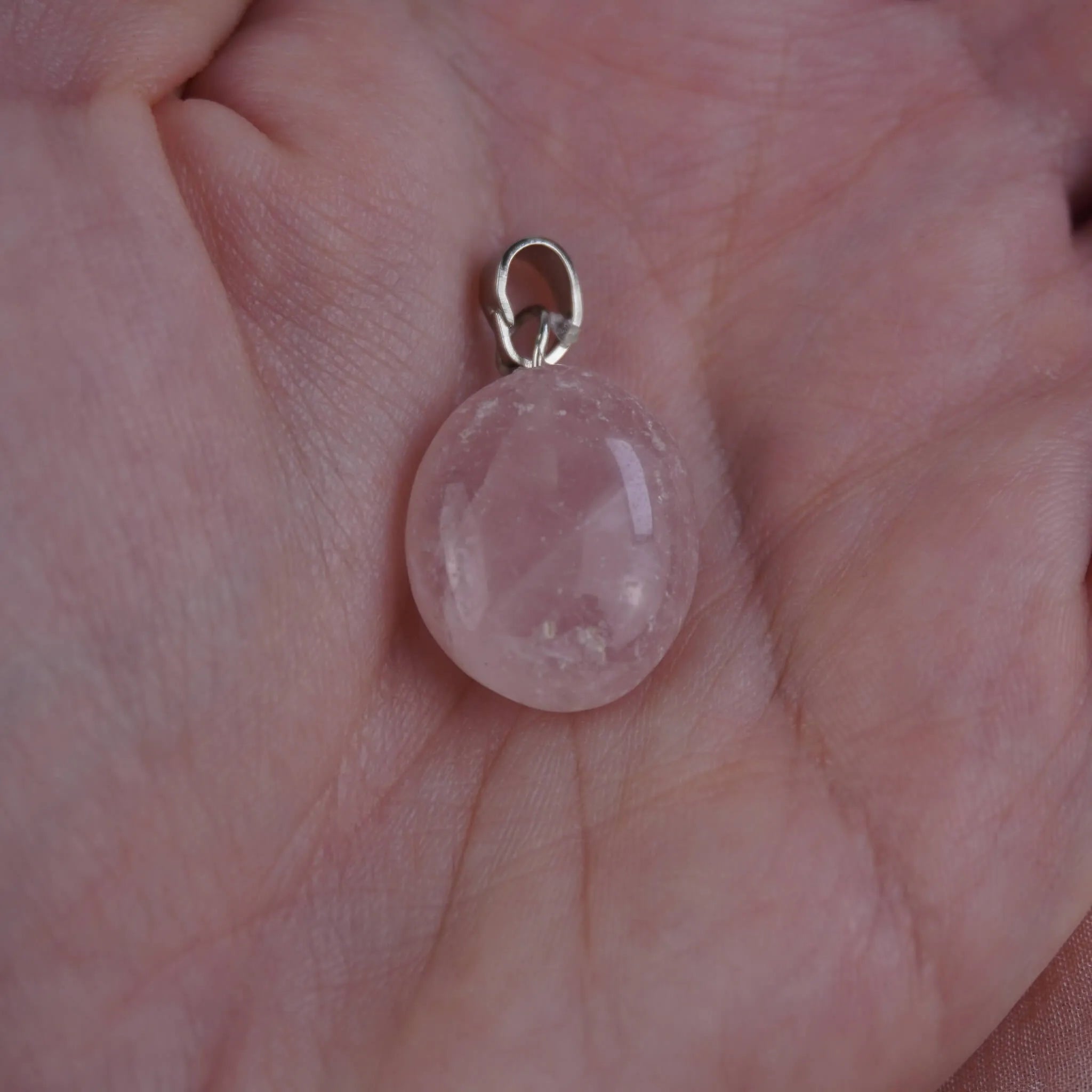 Rosenquarz Kettenanhänger mit silberfarbener Öse in einer Hand liegend