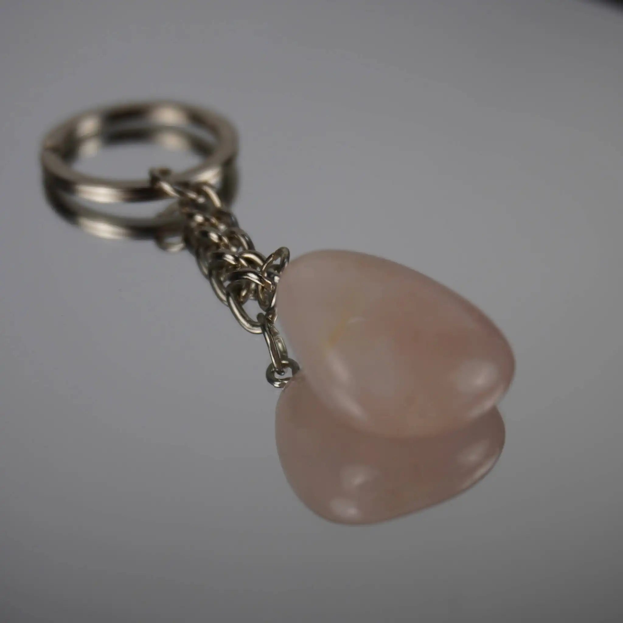 Rosenquarz Trommelstein Schlüsselanhänger mit Spiegelung auf Glasfläche