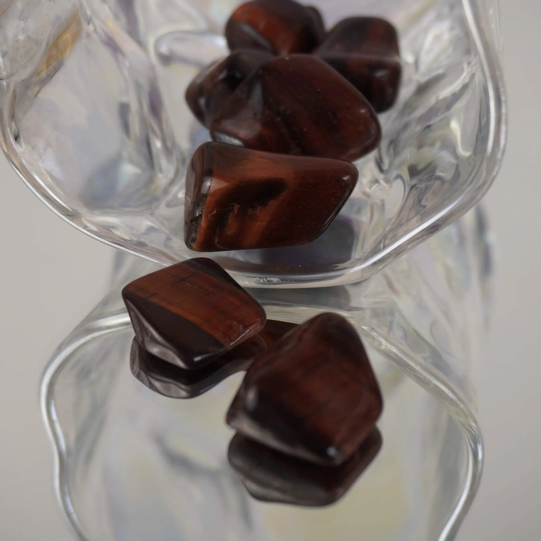 Mehrere rote Tigerauge Trommelsteine mit Spiegelung in transparenter Glasschale