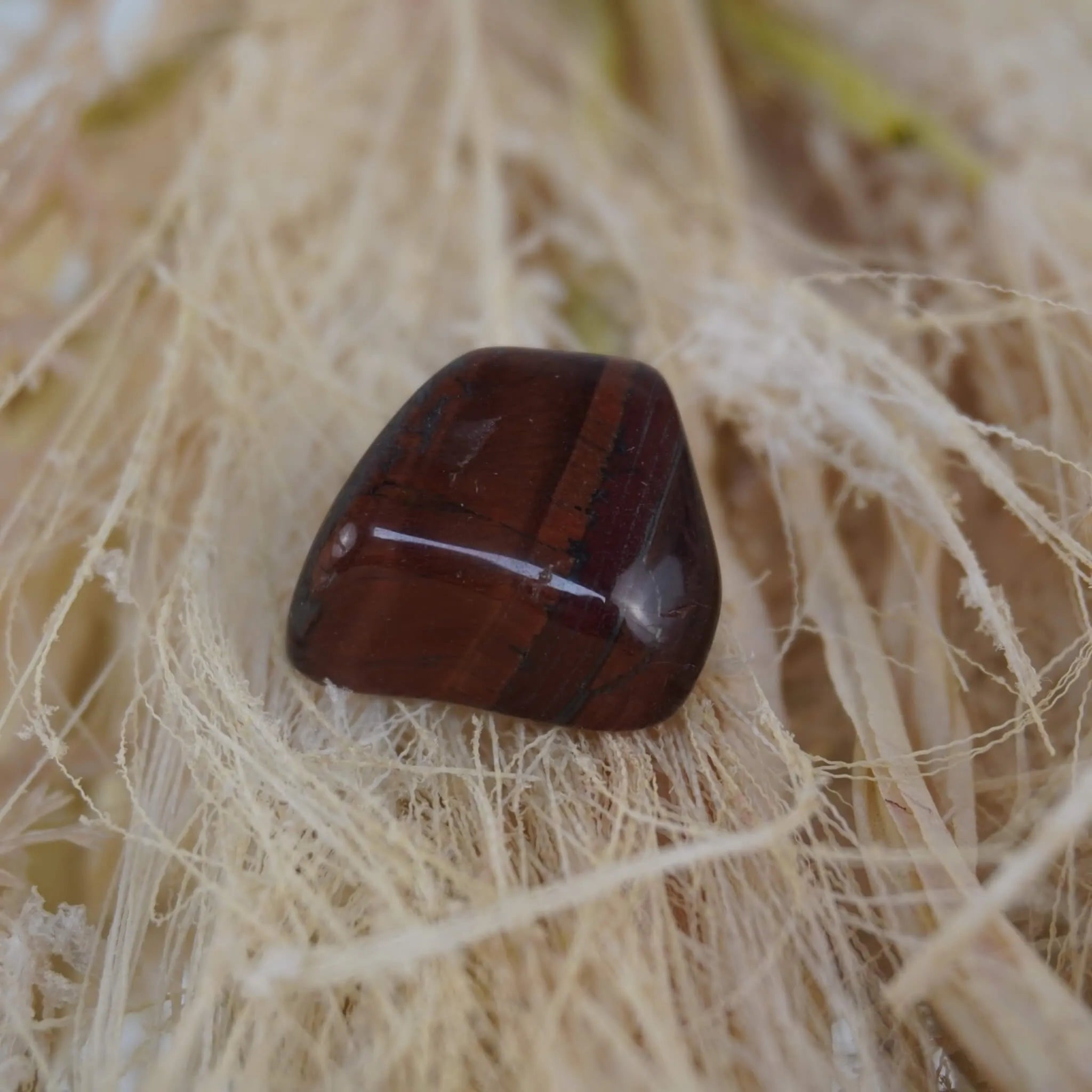 Roter Tigerauge Trommelstein mit Streifenzeichnung auf hellen Naturfasern