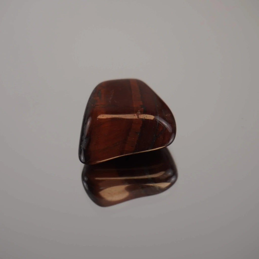 Ein einzelner roter Tigerauge Trommelstein mit Spiegelung auf glänzender Fläche