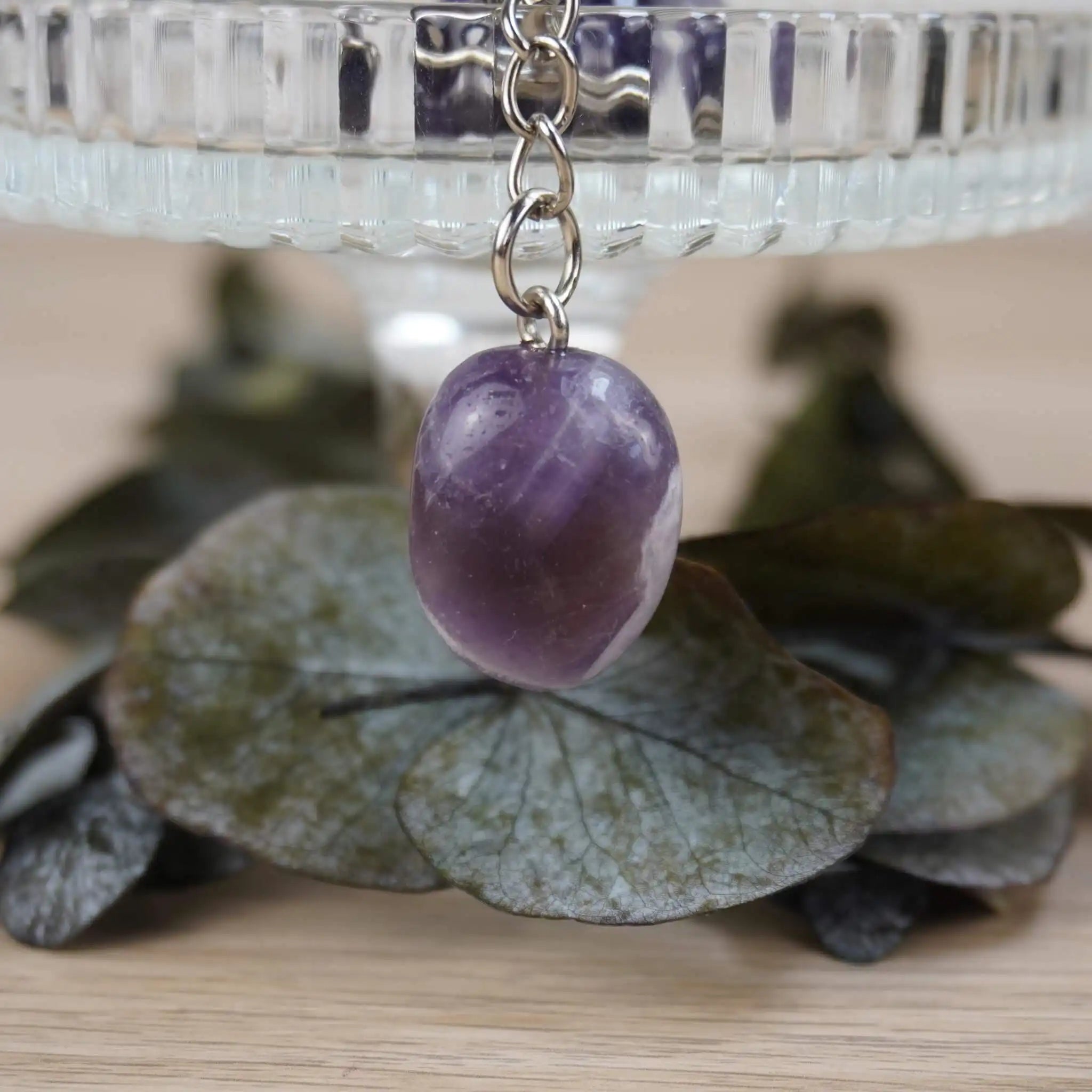 Amethyst Trommelstein Schlüsselanhänger vor Glasgefäß und Blätterdeko