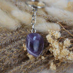 Schlüsselanhänger mit Amethyst Trommelstein auf getrocknetem Gras und Blüten