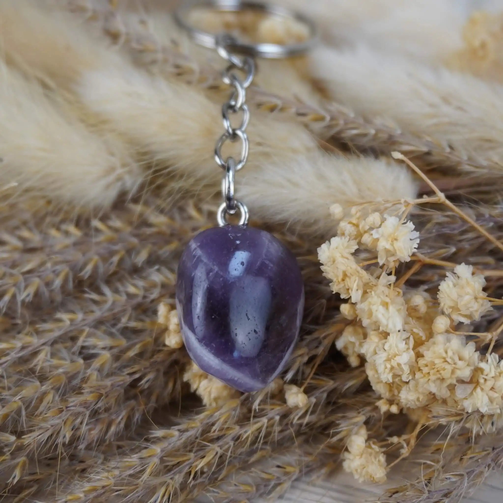 Schlüsselanhänger mit Amethyst Trommelstein auf getrocknetem Gras und Blüten