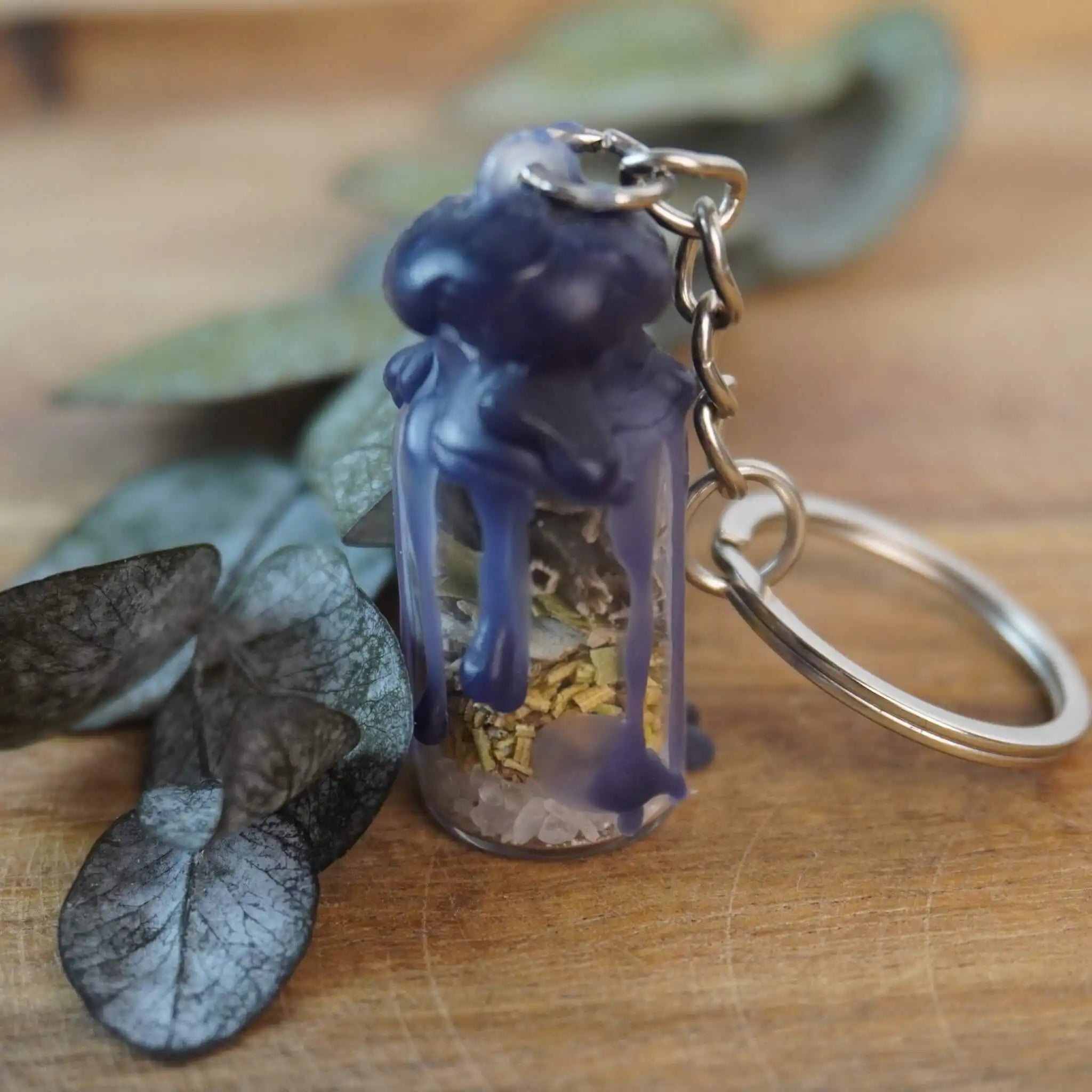 Protection Spell Jar Schlüsselanhänger mit Kräutern und Kristallen, eingefasst in dunklem Wachs, auf Holz mit Blättern