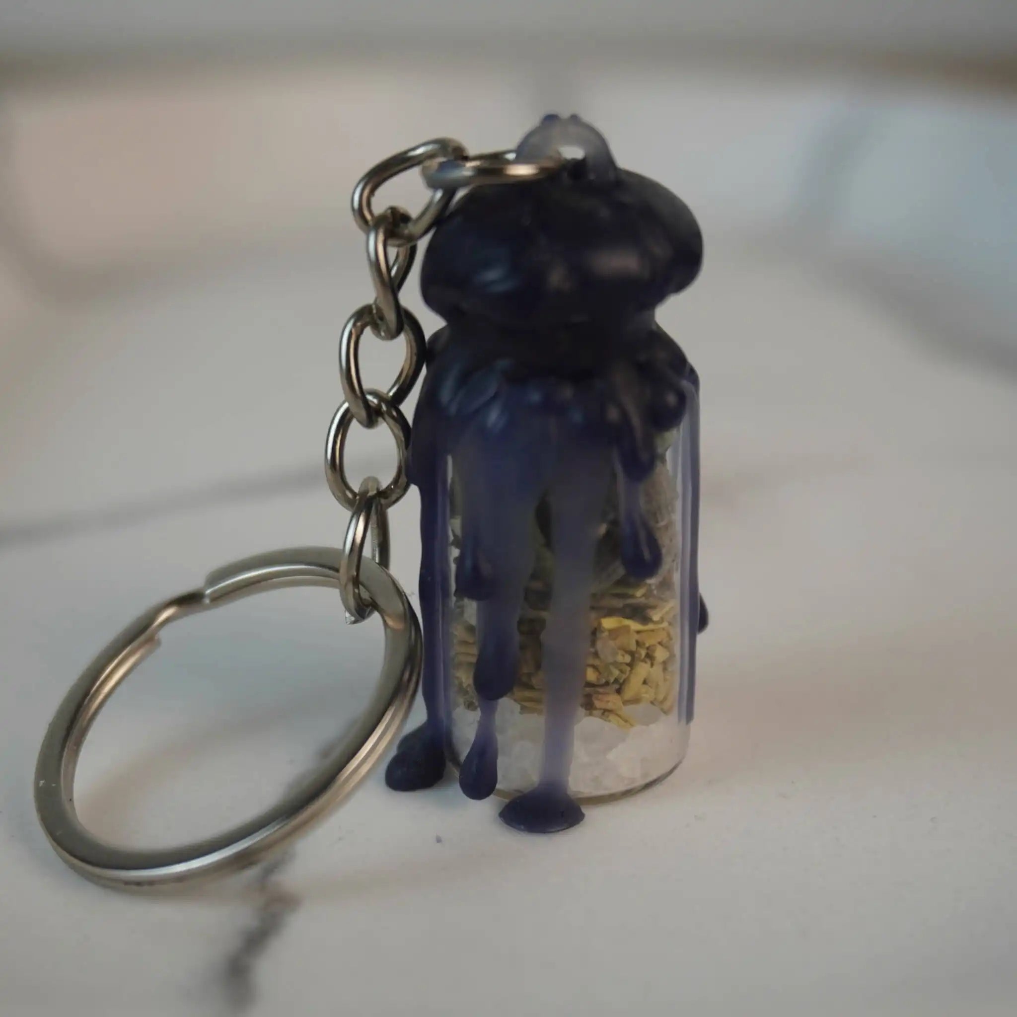 Protection Spell Jar Schlüsselanhänger mit dunklem Wachs und Kristallen, auf weißer Fläche