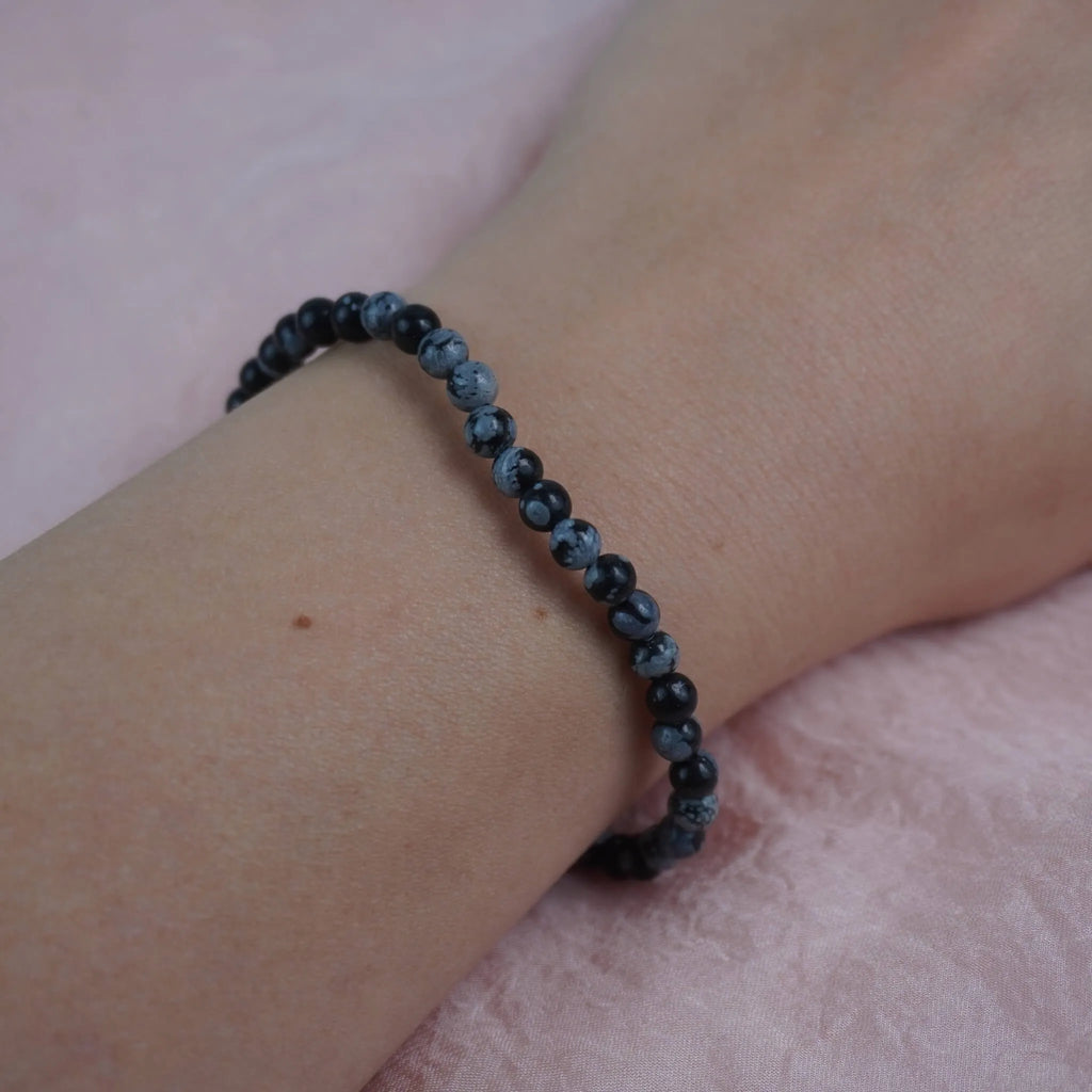 Schneeflocken Obsidian Kugelarmband dezent am Handgelenk vor rosa Hintergrund