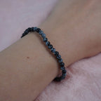 Schneeflocken Obsidian Kugelarmband dezent am Handgelenk vor rosa Hintergrund