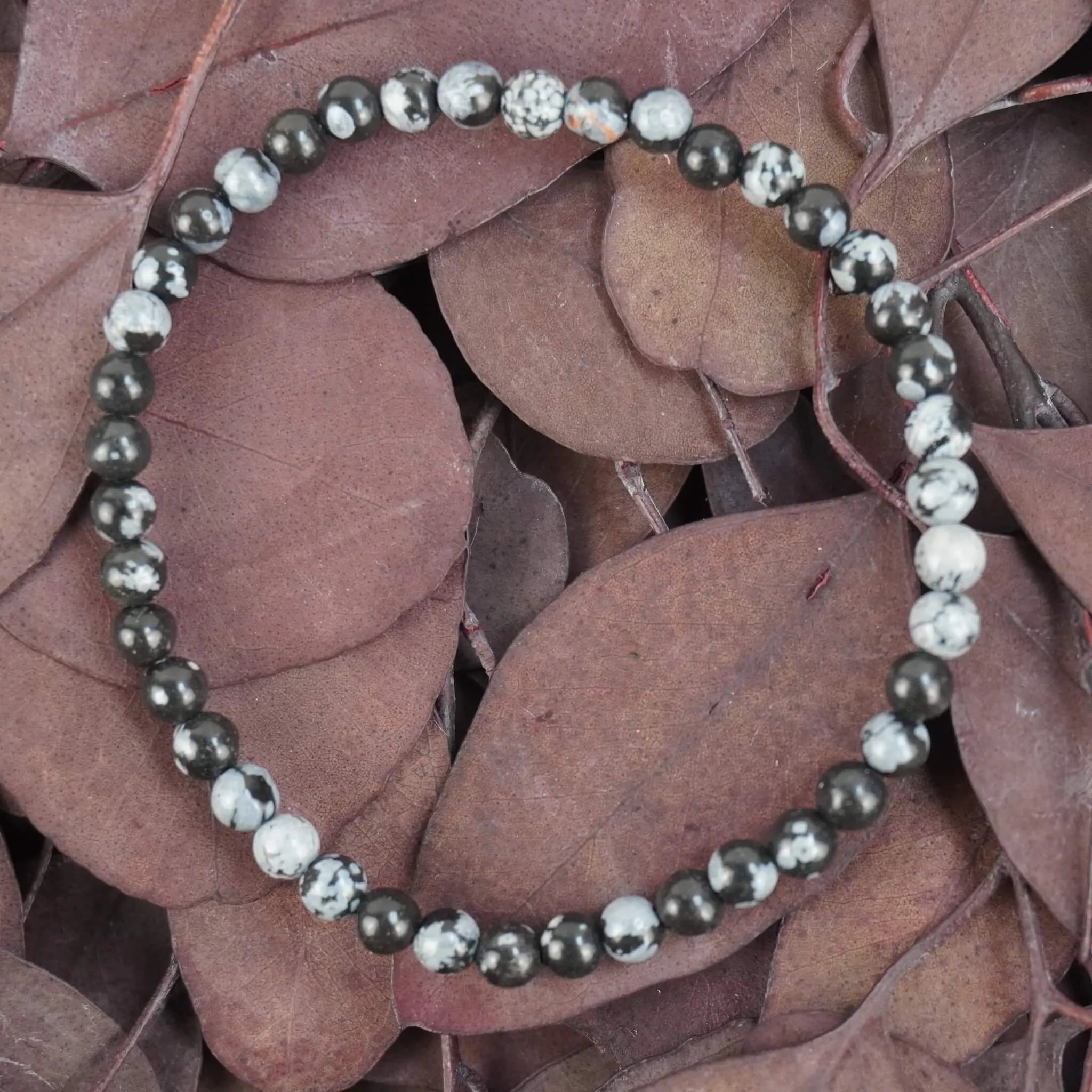 Schneeflocken Obsidian Kugelarmband auf violett-braunen Blättern natürlich arrangiert