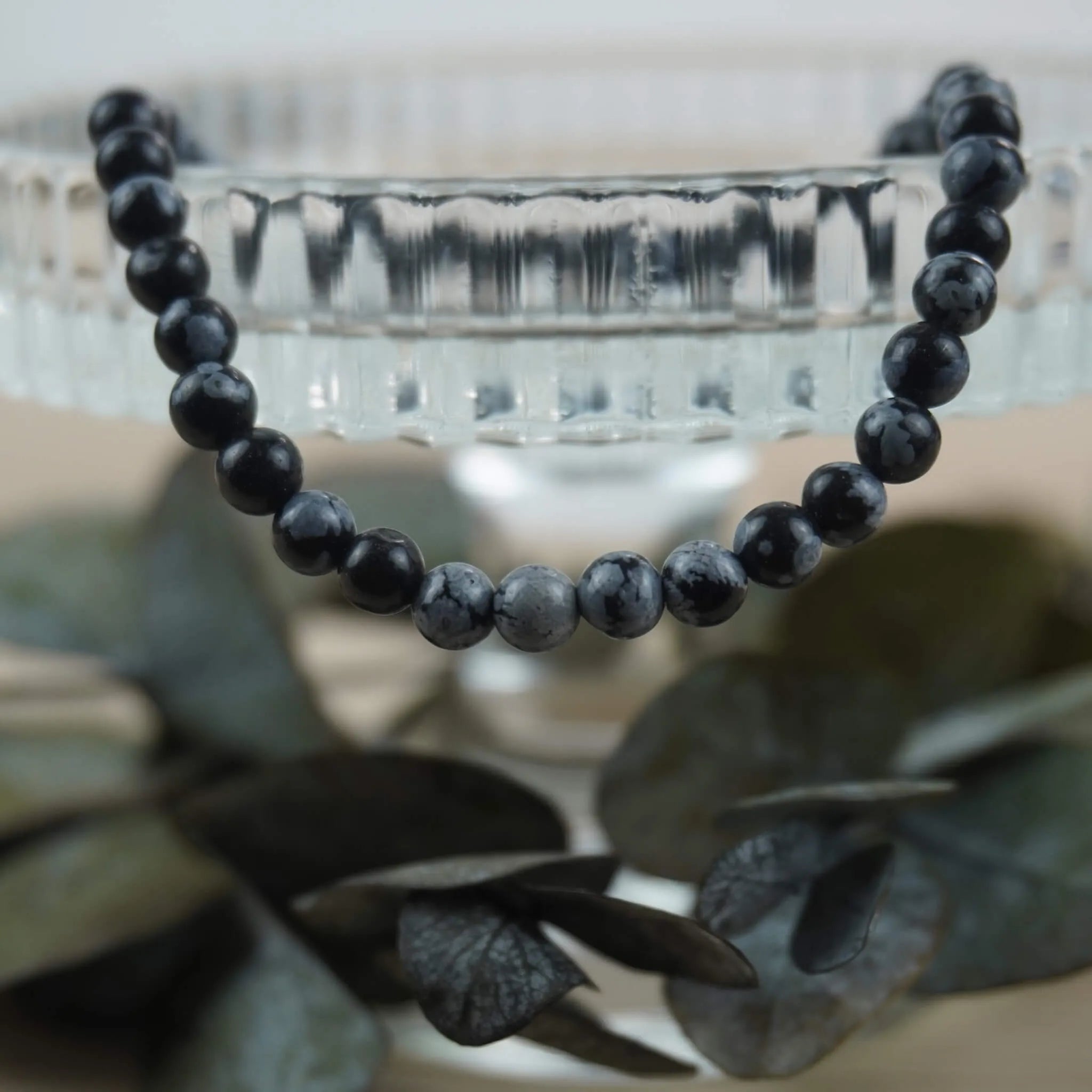 Schneeflocken Obsidian Kugelarmband  stilvoll dekoriert auf Glas-Schale mit Eukalyptus