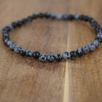 Schneeflocken Obsidian Kugelarmband im Nahaufnahme-Detail auf warmer Holzoberfläche