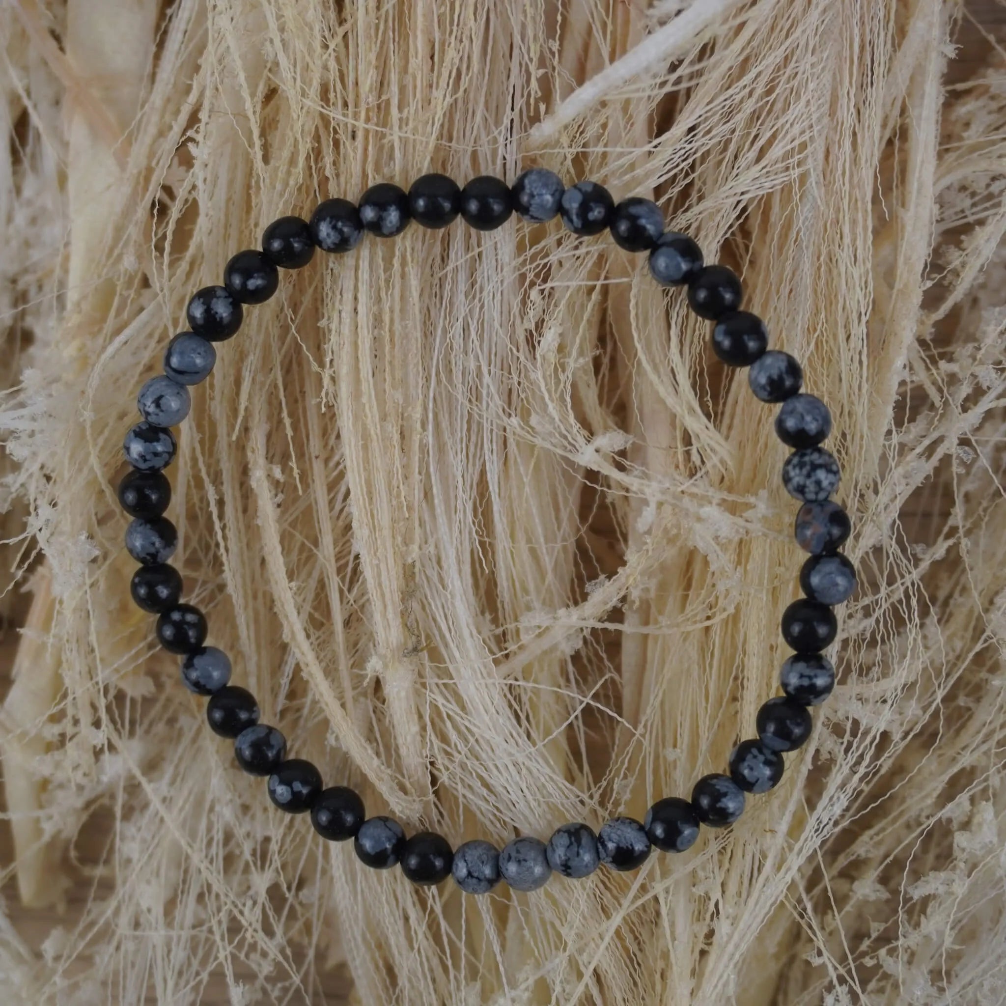 Schneeflocken Obsidian Kugelarmband auf hellem Naturfaserdekor mit sichtbarer Struktur