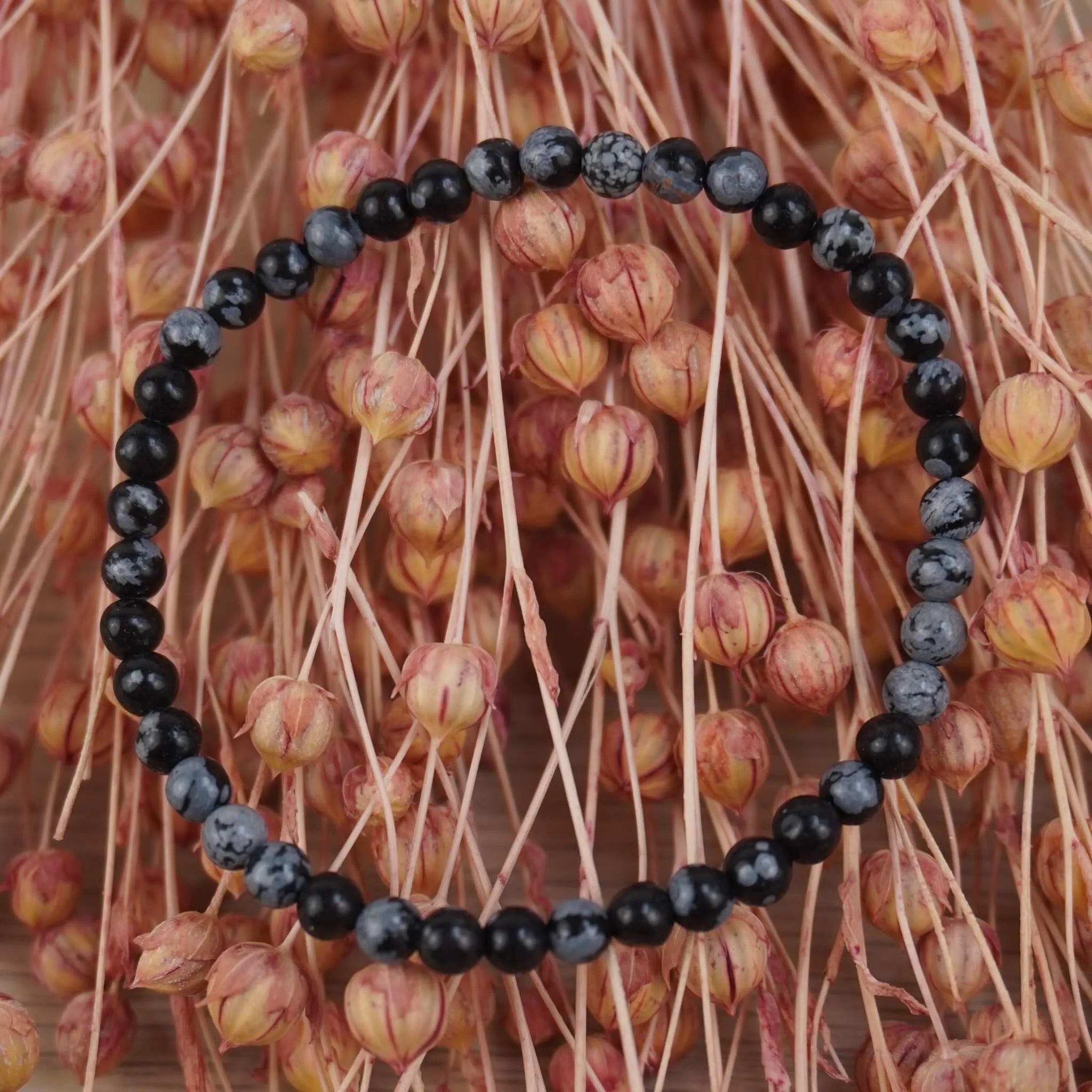 Schneeflocken Obsidian Kugelarmband vor rosafarbenen Trockenblumen mit Kontrast