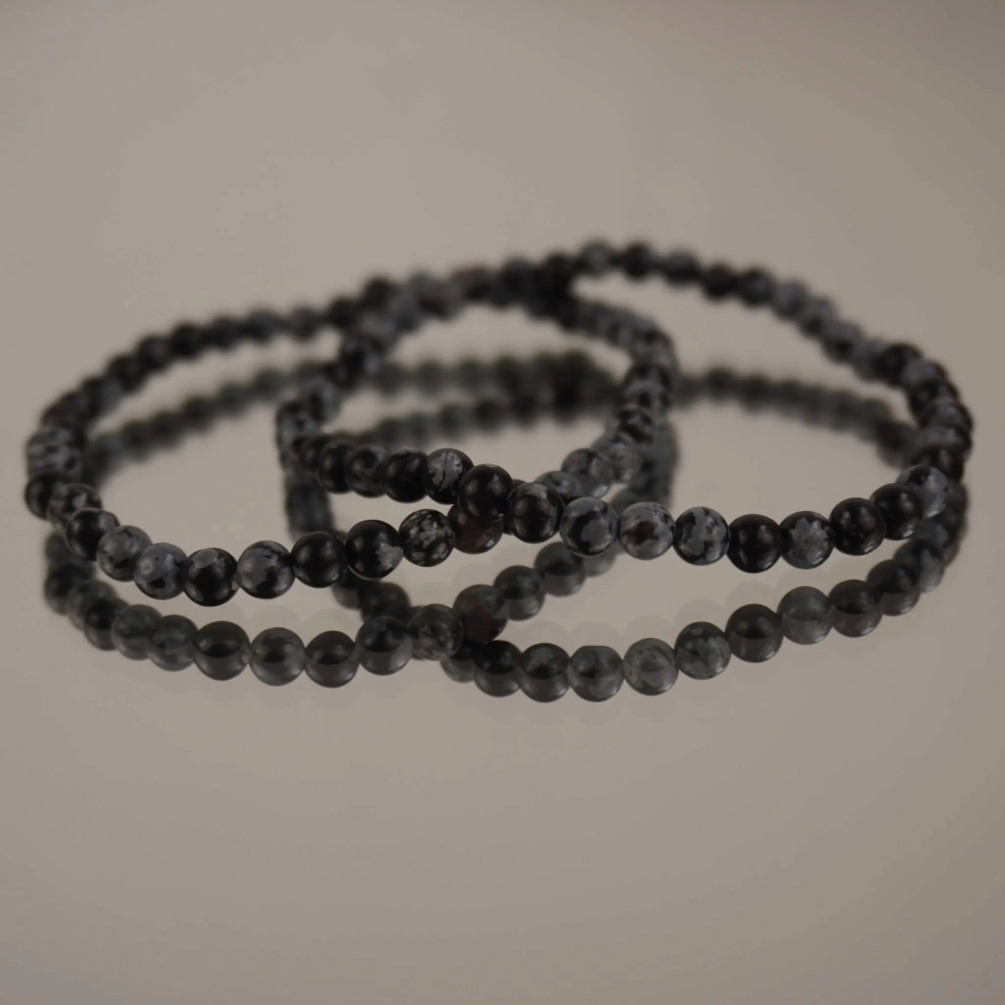 Schneeflocken Obsidian Kugelarmband auf spiegelnder Fläche mit eleganter Reflexion