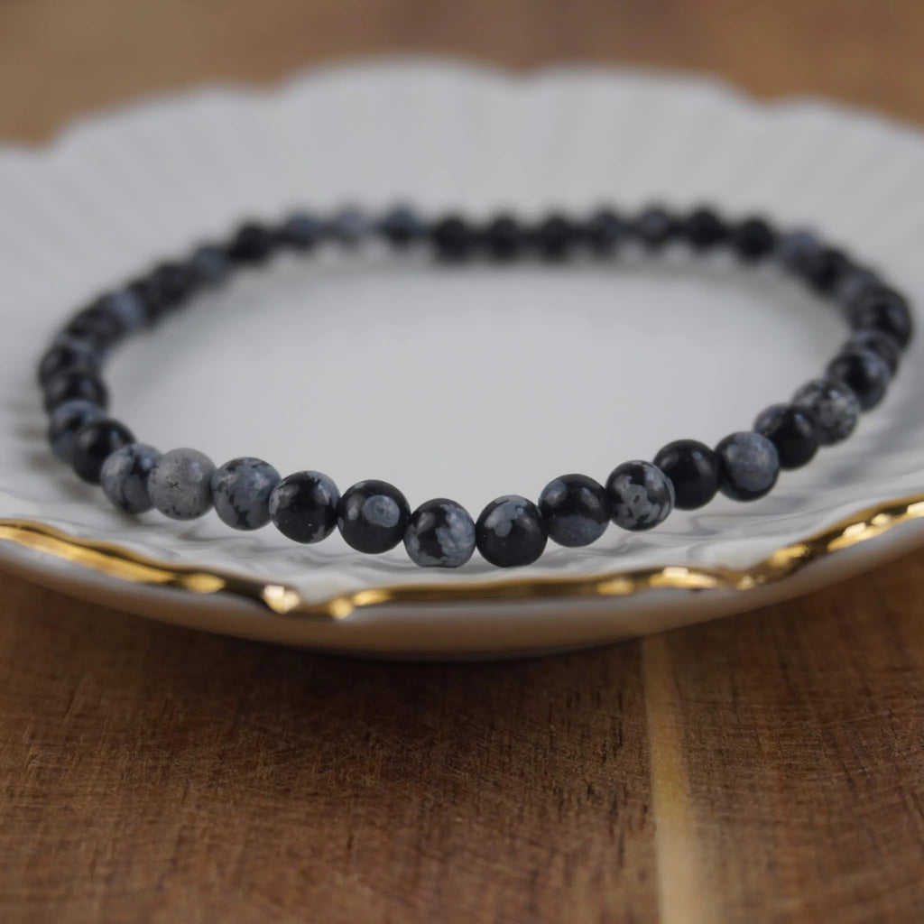 Schneeflocken Obsidian Kugelarmband auf weißem Teller mit feinem Goldrand