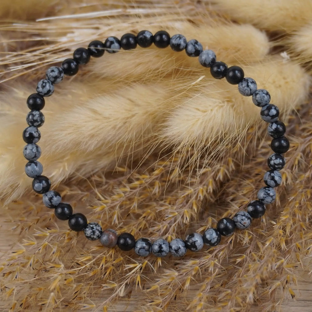 Schneeflocken Obsidian Kugelarmband auf beigen Trockenblumen im modernen Boho-Stil