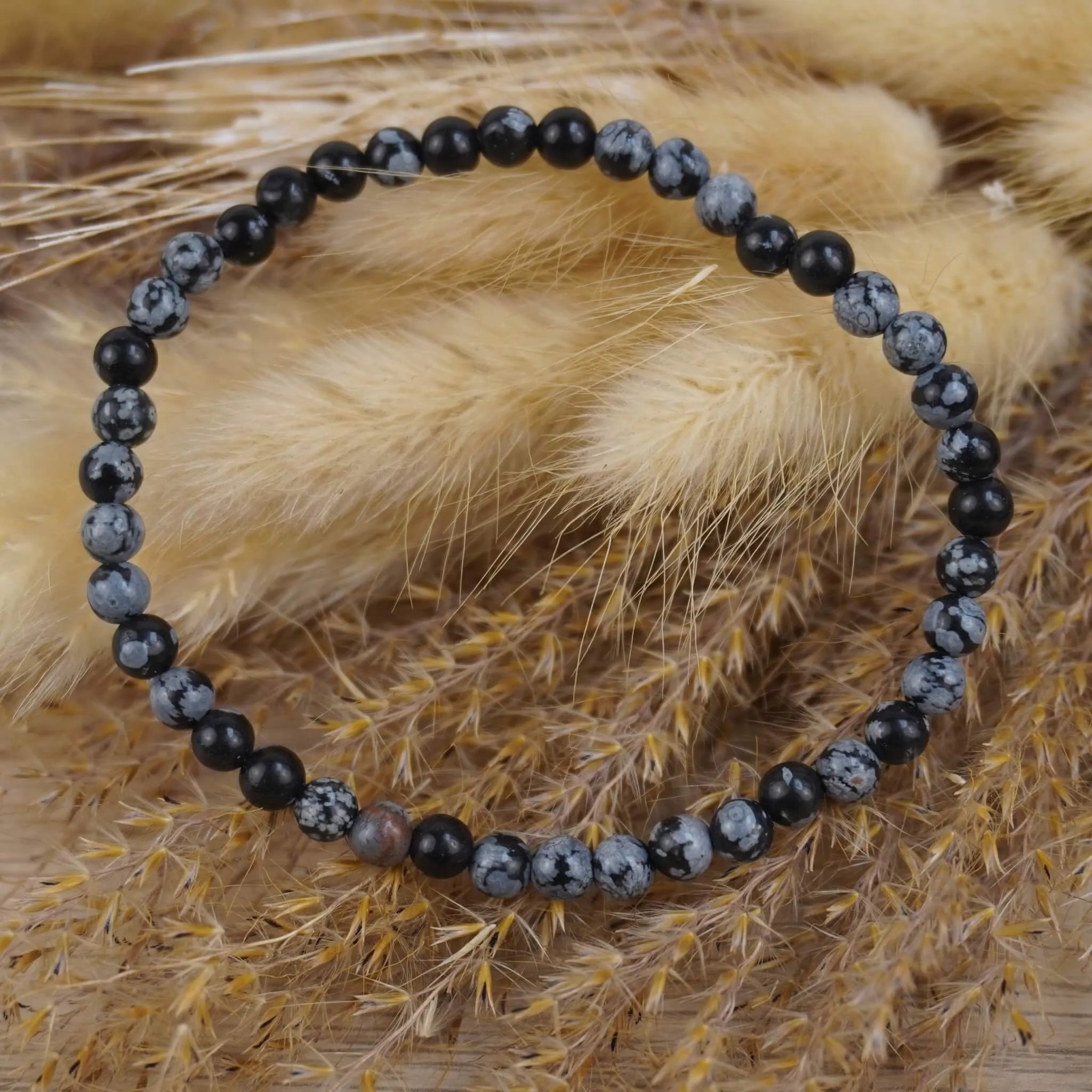 Schneeflocken Obsidian Kugelarmband auf beigen Trockenblumen im modernen Boho-Stil