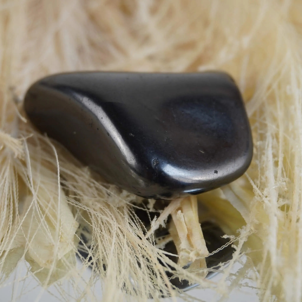 Schungit Trommelstein arrangiert auf hellen Naturfasern