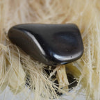 Schungit Trommelstein arrangiert auf hellen Naturfasern