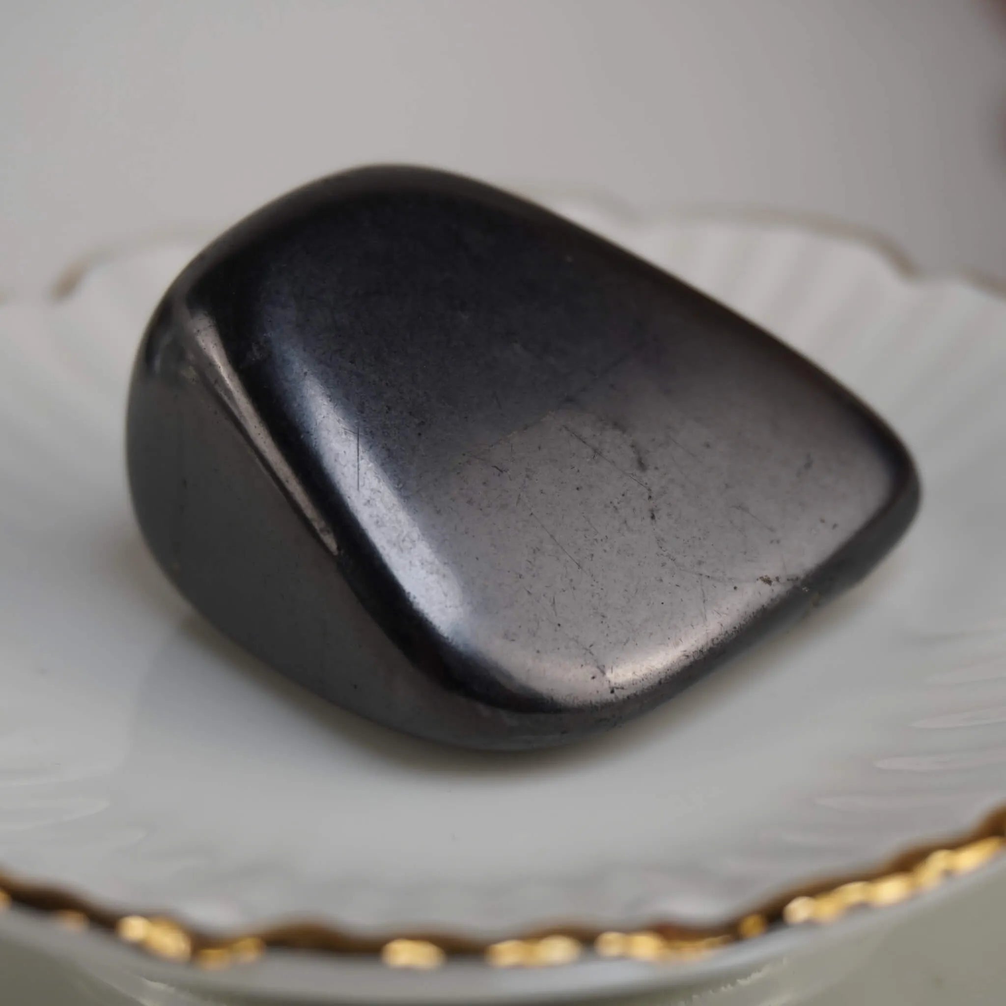 Polierter schwarzer Schungit Trommelstein auf weißer Schale mit Goldrand