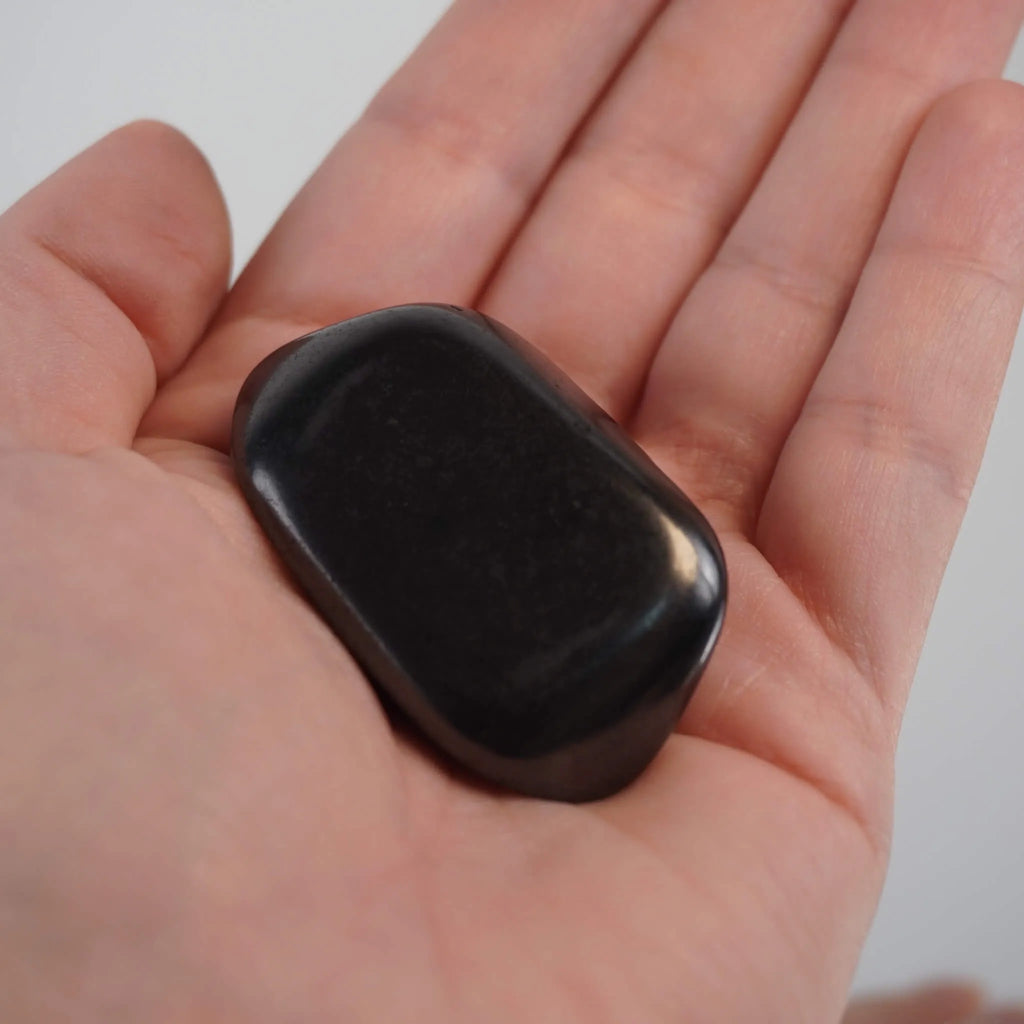 Schungit Trommelstein in einer geöffneten Hand gehalten