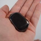 Schungit Trommelstein in einer geöffneten Hand gehalten