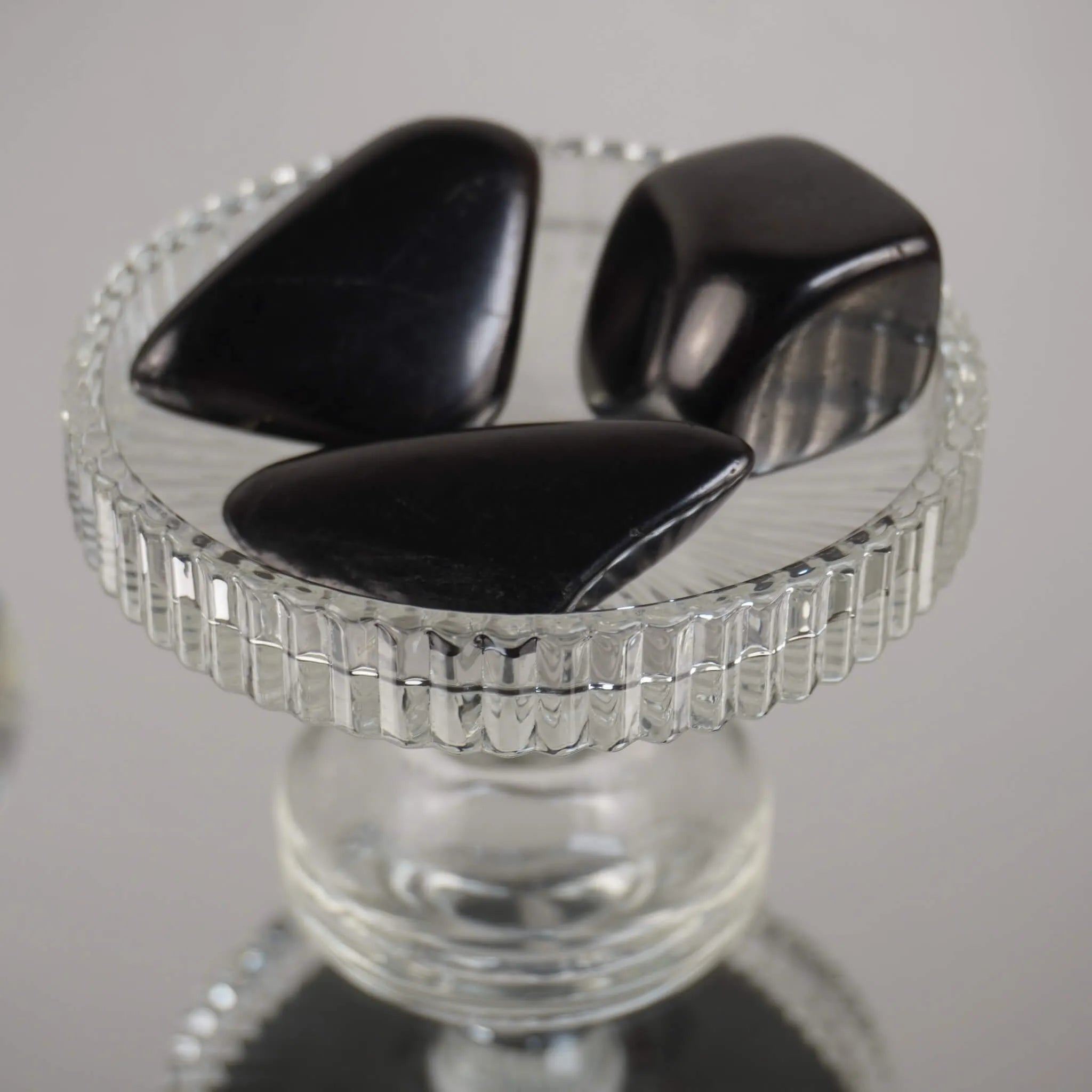 Drei dunkle Schungit Trommelsteine dekorativ auf klarem Glaskelch arrangiert