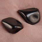 Zwei Schungit Trommelsteine präsentiert auf zart rosafarbenem Stoff