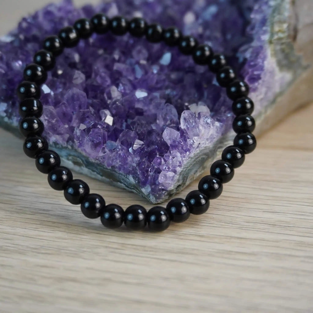 Schwarzer Turmalin Kugelarmband vor Amethyst-Kristall Dekoration