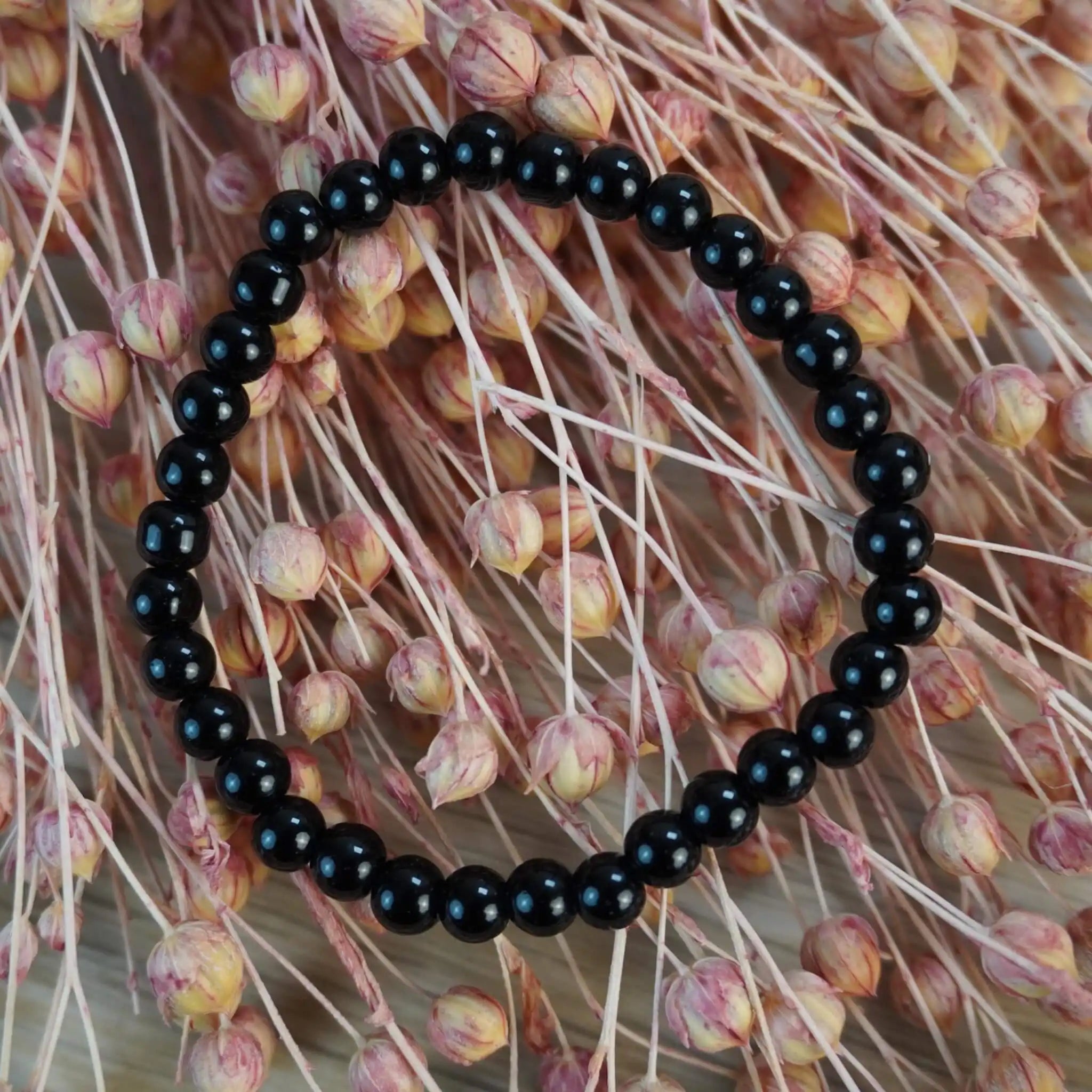Schwarzer Turmalin Kugelarmband mit rosa Trockenblumen im Hintergrund