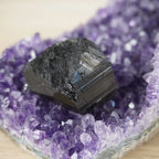 Schwarzer Turmalin Rohstein auf einer Amethystdruse