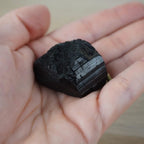 Schwarzer Turmalin Rohstein liegt auf einer Handfläche