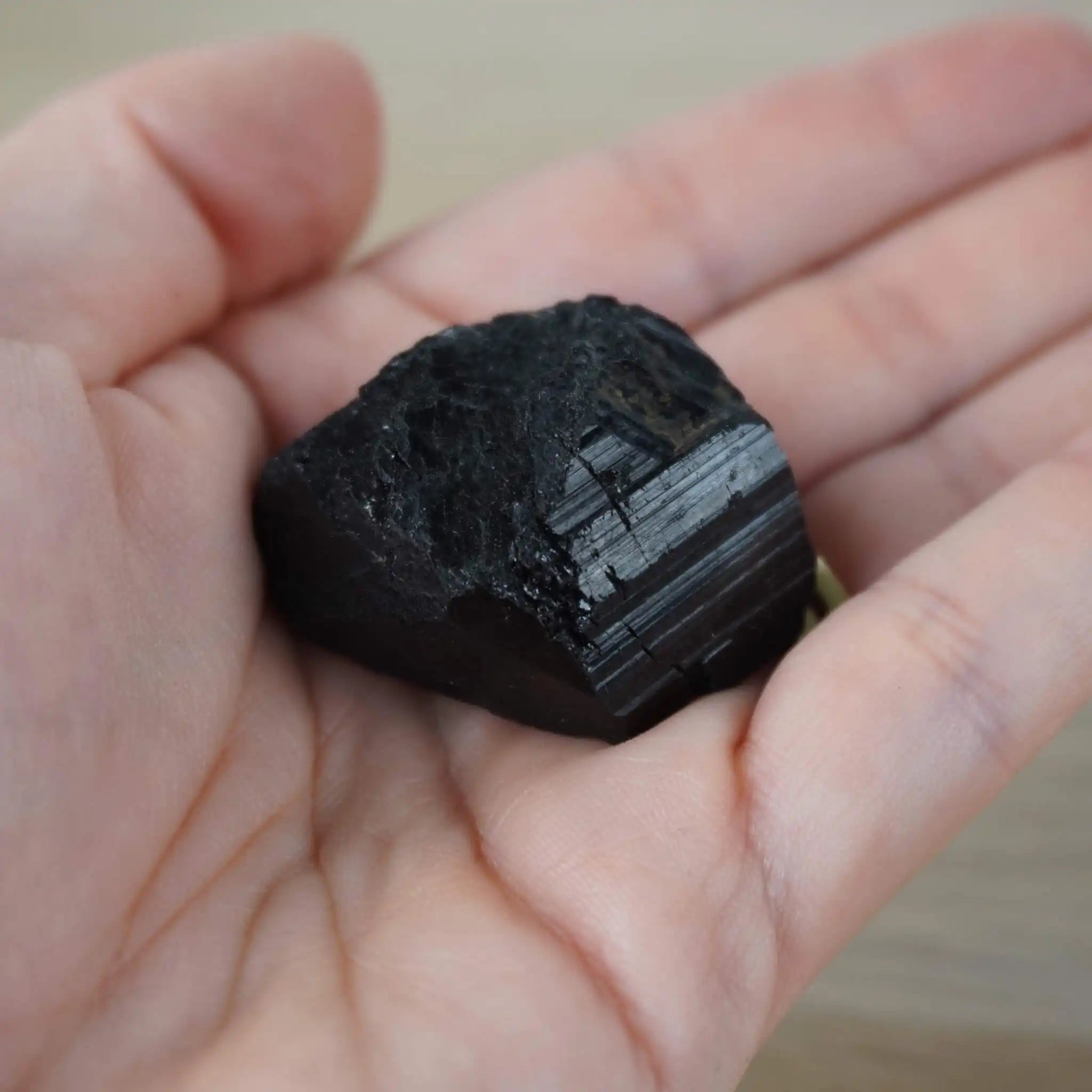Schwarzer Turmalin Rohstein liegt auf einer Handfläche