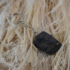 Schwarzer Turmalin Schlüsselanhänger arrangiert auf hellen Naturfasern