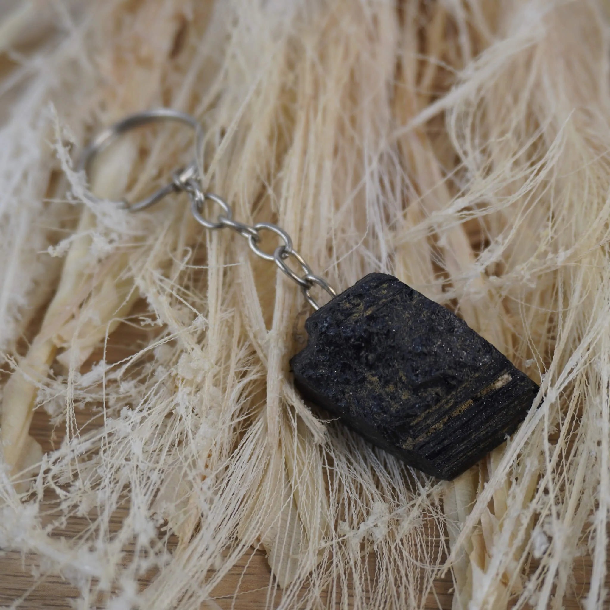 Schwarzer Turmalin Schlüsselanhänger arrangiert auf hellen Naturfasern