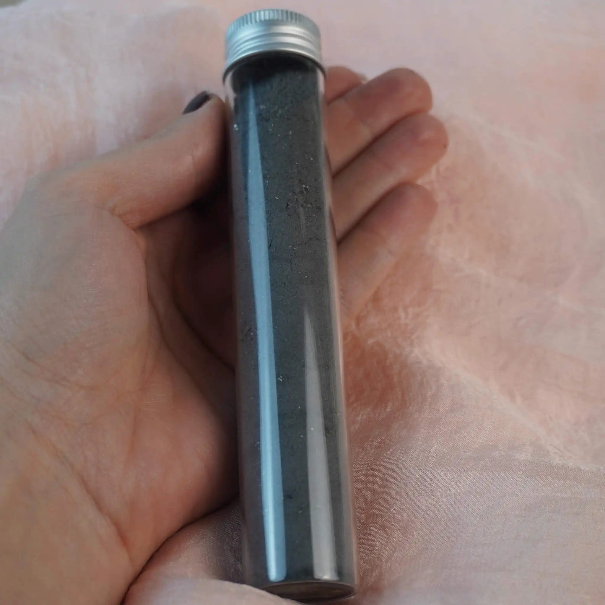 Schwarzes Dekosalz im Glasröhrchen in einer Hand gehalten