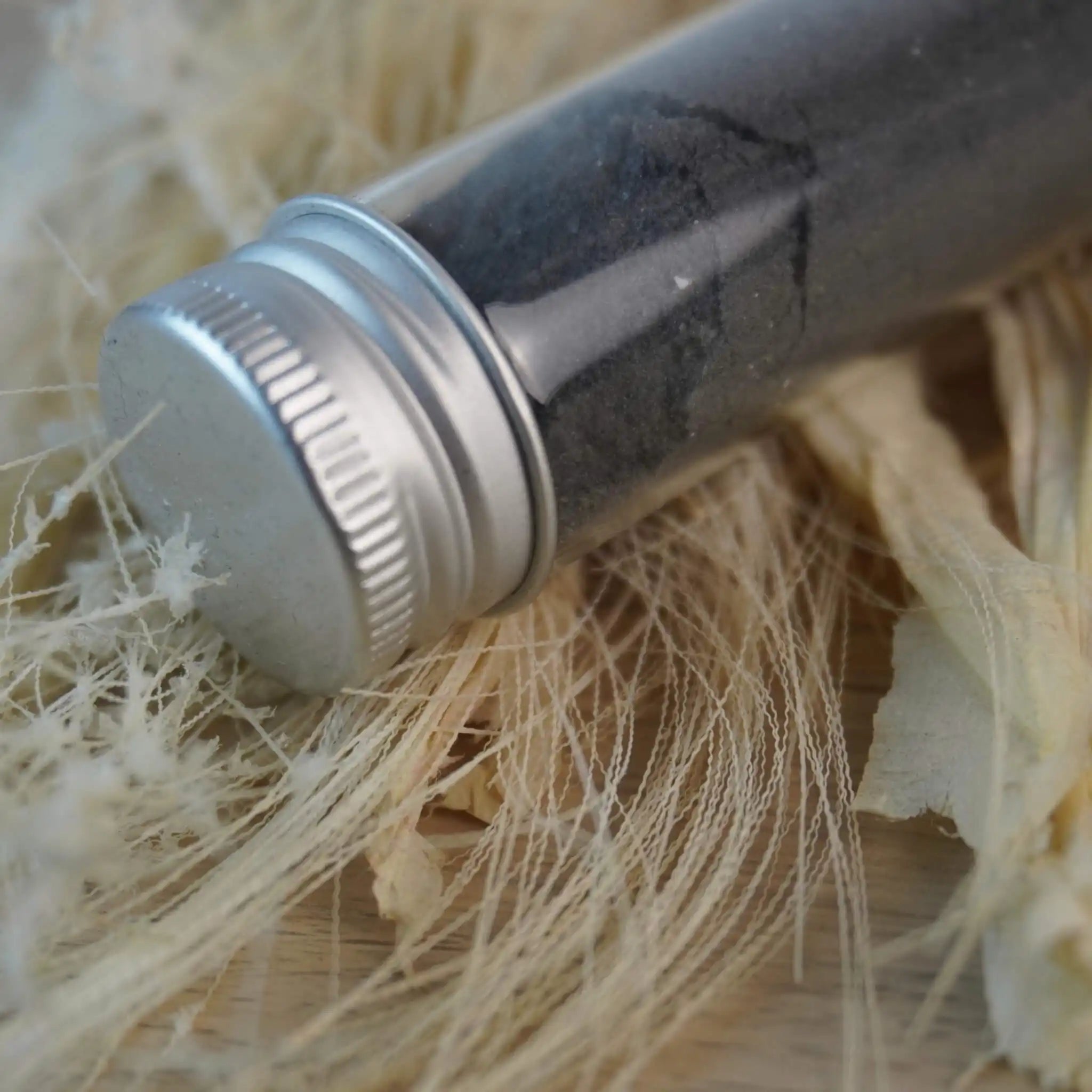 Nahaufnahme eines Glasröhrchens mit schwarzem Dekosalz auf Naturfasern
